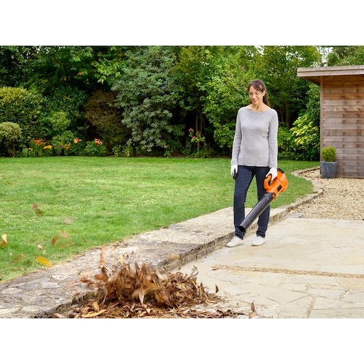 BLACKDECKER BCBL200B leaf blower used in garden, person clearing dry leaves on stone path.