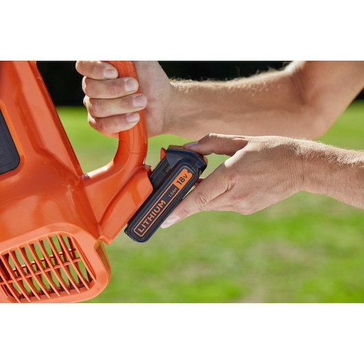 BLACKDECKER BCBL200L battery being inserted in orange leaf blower, close-up outdoor view.