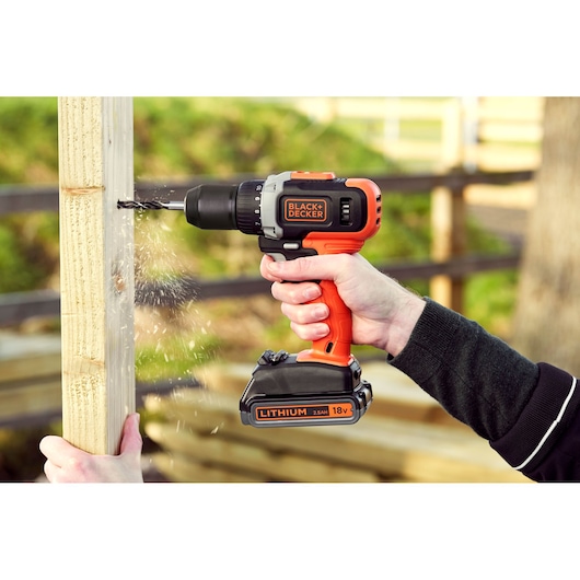 BLACKDECKER BCD002ME2K cordless drill with 18V lithium battery drilling into wood, handheld in outdoor setting.