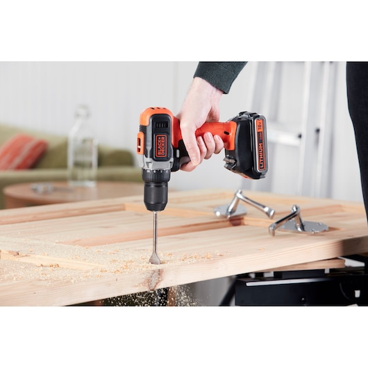 BLACK+DECKER BCD002ME2K cordless drill in use drilling wood, side view, visible sawdust.