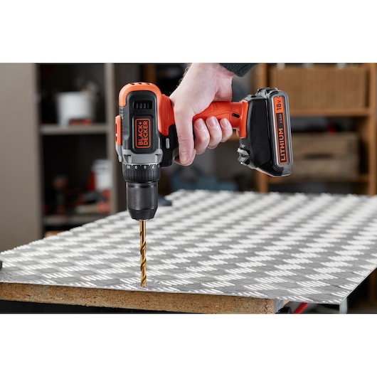 BLACK+DECKER BCD002ME2K cordless drill used on metal sheet, close-up side view.