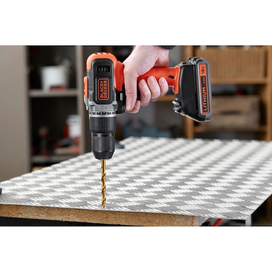 BLACK+DECKER BCD003ME2K cordless drill with 18V lithium battery drilling into metal sheet, handheld side view.