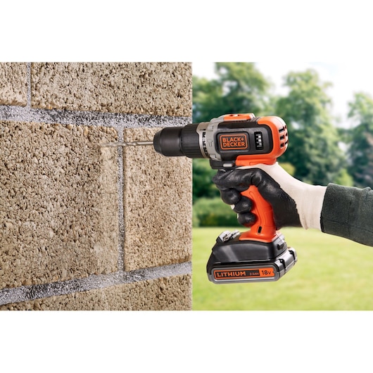 BLACKDECKER BCD003ME2K cordless drill used on concrete wall outdoors, orange and black body.