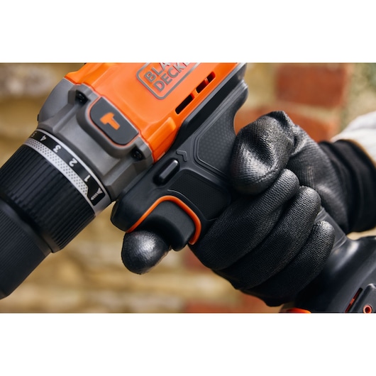 BLACK+DECKER BCD383D1 cordless drill close-up, black and orange design, gloved hand holding handle.
