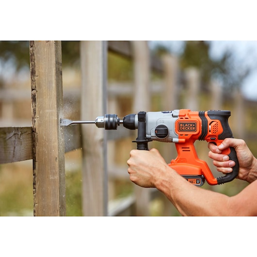 Photo of BLACK+DECKER BCD900E2K cordless hammer drill in use, drilling wood outdoors.