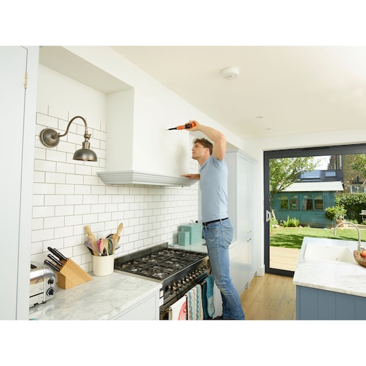 BLACKDECKER BCF602C cordless screwdriver in use on white kitchen wall above stove.