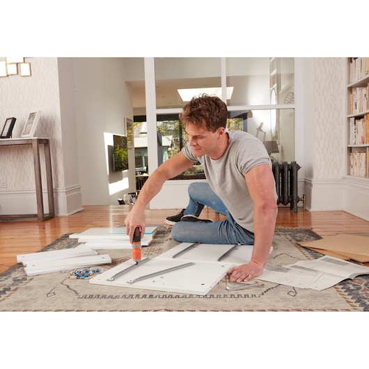 BLACKDECKER BCF602C cordless screwdriver used for furniture assembly on a rug in a modern living room.