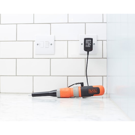 BLACK+DECKER BCF602C orange and black cordless screwdriver charging on countertop against white tile wall.