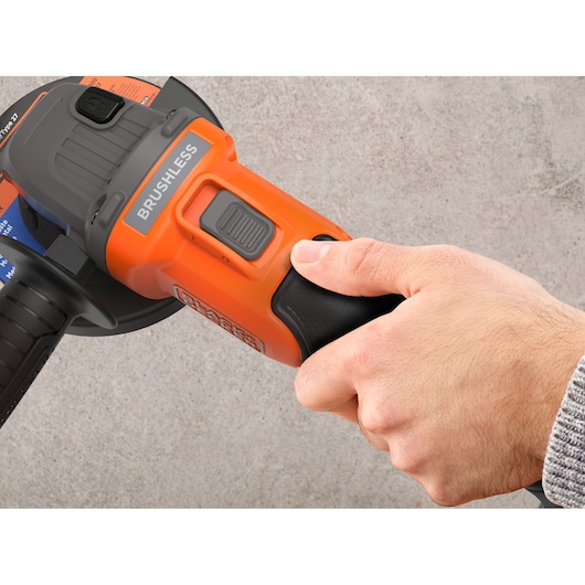 BLACKDECKER BCG6L8F1S angle grinder close-up, hand pressing power switch, orange body, grey brushless motor.