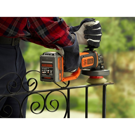 BLACKDECKER BCG720M1 cordless angle grinder used on metal railing outdoors, orange and black design.