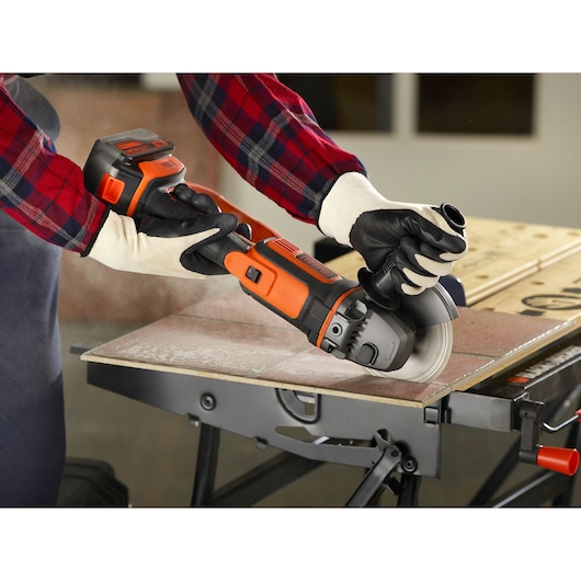 BLACKDECKER BCG720M1 cordless angle grinder in use cutting tile on workbench.