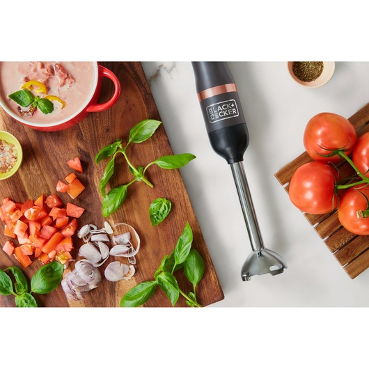 BLACK+DECKER BCKM1011KGF hand blender on a kitchen counter with fresh tomatoes, basil, and chopped vegetables.