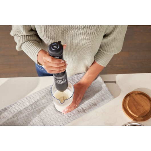 Photo of BLACKDECKER BCKM1012KB hand blender mixing liquid in a transparent measuring cup on kitchen counter.