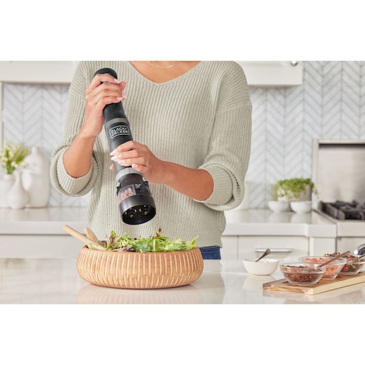 Photo of person using BLACK+DECKER BCKM1012KB electric grinder over salad in modern kitchen.