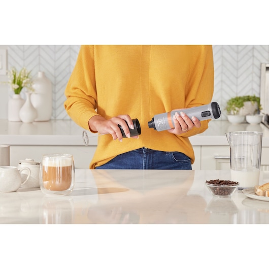 BLACKDECKER BCKM1012KG milk frother held in hand on kitchen counter with coffee and accessories.