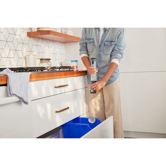 Photo of BLACKDECKER BCKM1012KG handheld vacuum cleaning near a kitchen counter and blue recycling bin.