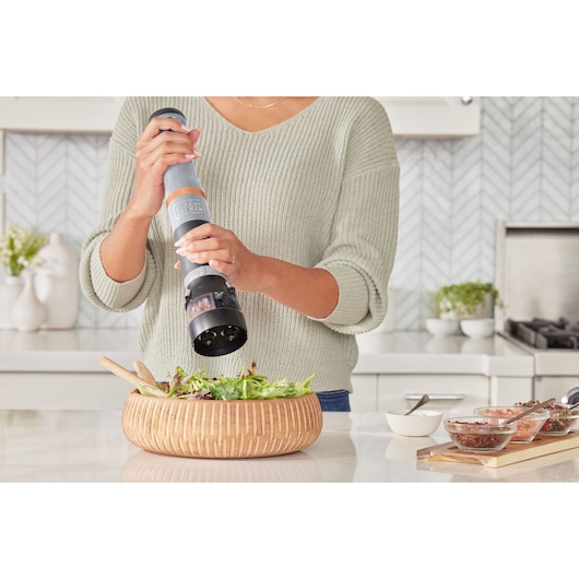 Photo of BLACK+DECKER electric pepper grinder BCKM1012KG being used to season a salad in a wooden bowl.