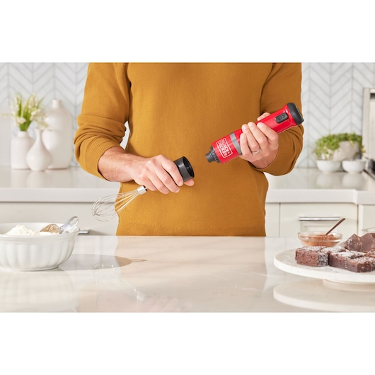 BLACKDECKER BCKM1012KR cordless hand mixer, red, held in kitchen preparing to attach whisk accessory.