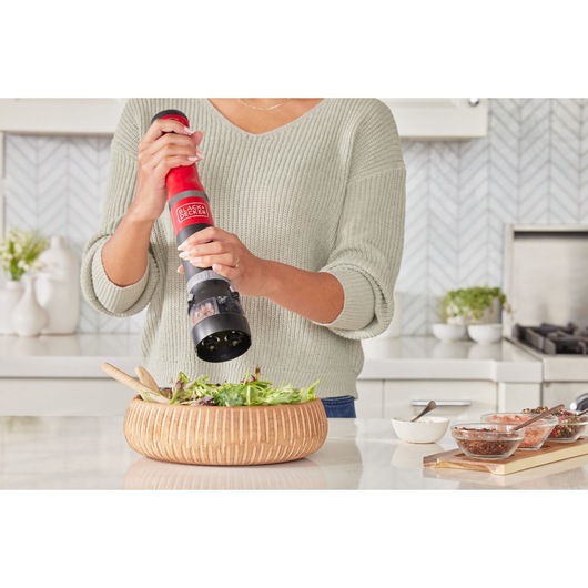 Photo of a person using a BLACKDECKER electric pepper grinder BCKM1012KR to season a salad in a wood bowl.