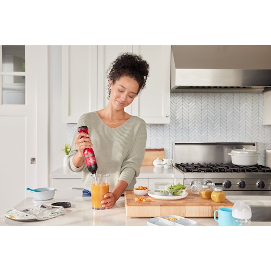 BLACKDECKER BCKM1012KR hand blender blending orange liquid in glass in modern kitchen setting.