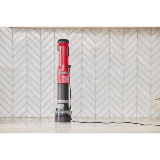 BLACKDECKER BCKM1012KR stick vacuum cleaner in red and black, upright on a kitchen counter with cord visible.