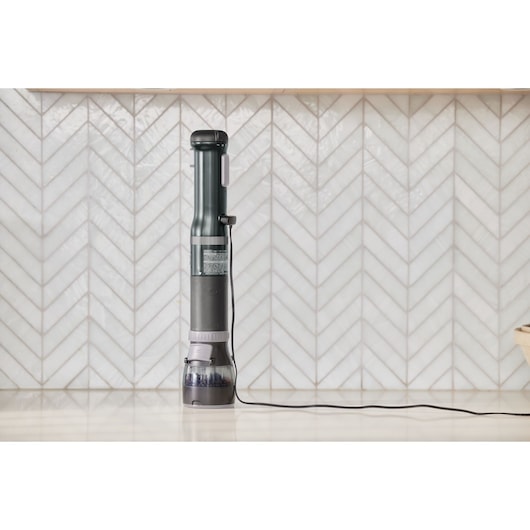 BLACKDECKER BCKM1016KSB handheld vacuum cleaner upright on a kitchen counter, cord visible, tile backsplash.