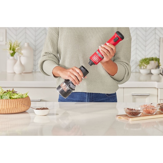 Photo of a person using a BLACKDECKER BCKM1016KSR electric grinder in a kitchen, preparing food on a counter.