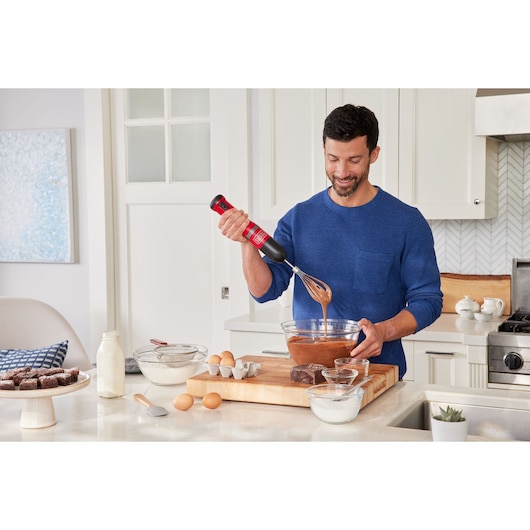 Photo of a person using a BLACKDECKER BCKM1016KSR cordless hand mixer to mix batter in a glass bowl on a kitchen counter.