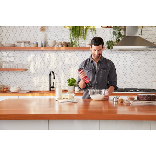 BLACKDECKER BCKM1016KSR mixer held by person in modern kitchen, mixing batter in glass bowl.