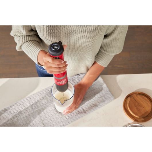 Photo of BLACKDECKER BCKM101MFFF red hand blender mixing liquid in a glass jug on a kitchen counter.