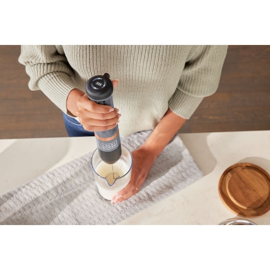 Photo of BLACK+DECKER BCKM101MFFF hand blender being used to mix ingredients in a clear jug on a kitchen counter.