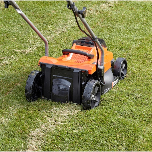 BLACKDECKER BCMW33184L2 orange cordless lawn mower on grass, rear view, showing wheels and handles.