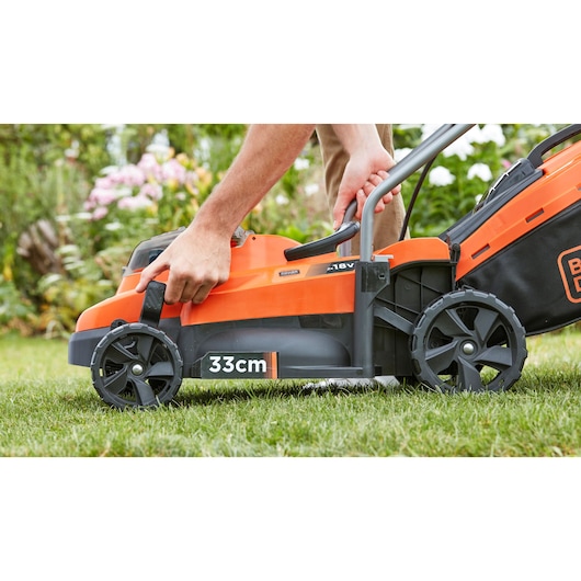 Photo of BLACK+DECKER BCMW3318L2 lawn mower, side view on grass, orange and black with 33cm cutting width.