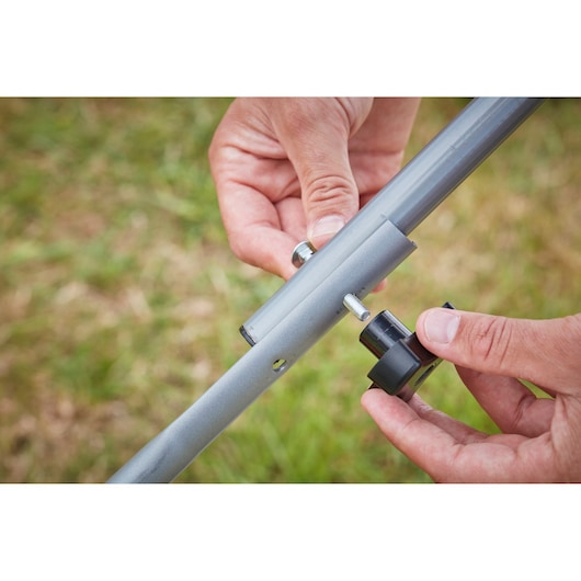 Close-up photo of hands assembling BLACK+DECKER BCMW3318L2 lawn mower handle with screw and black knob.
