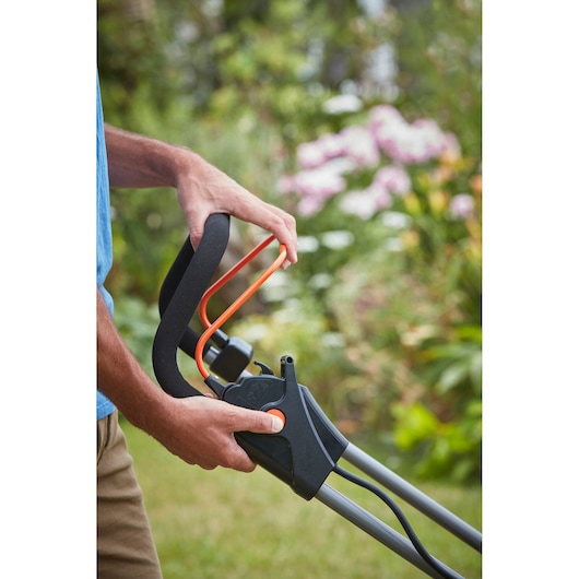 BLACKDECKER BCMW3318L2 lawn mower handle close-up, black and orange detail, in use outdoors.