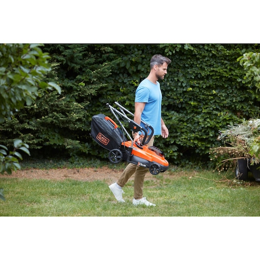 Photo of BLACKDECKER BCMW3336L1 lawn mower with folding handle carried by person in garden.