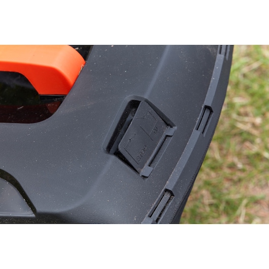 Close-up photo of BLACK+DECKER BCMW3336L1 lawn mower stop switch on black plastic surface.