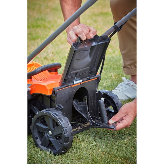 Photo of a BLACK+DECKER BCMW3336L1 lawn mower, close-up of a person opening the rear flap and compartment.