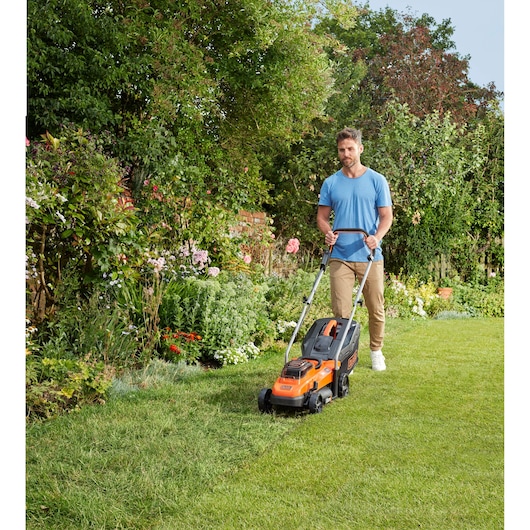 BLACKDECKER BCMW3336L2 lawn mower in use on grass in a garden, user pushing the orange and black mower forward.