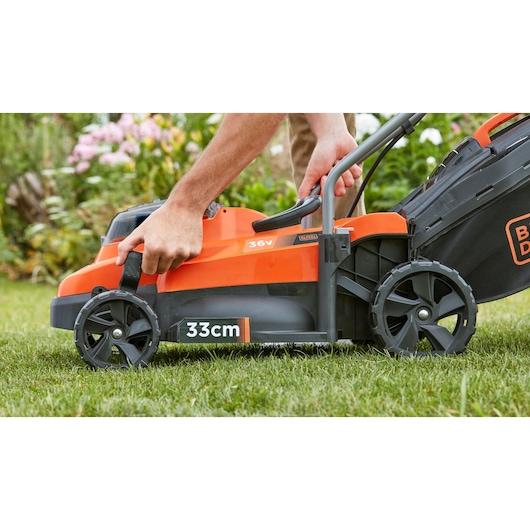 Photo of BLACKDECKER BCMW3336L2 lawn mower side view, 33cm blade, person adjusting wheel height.
