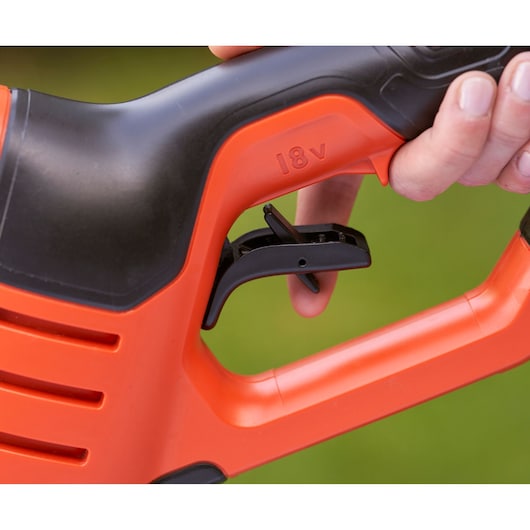 Close-up of a hand holding the handle of an orange and black BLACK+DECKER power tool, showing the trigger and the '18V' marking.