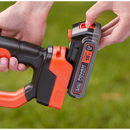 Close-up view of hands attaching an 18V lithium battery to a BLACK+DECKER power tool with orange and black casing.