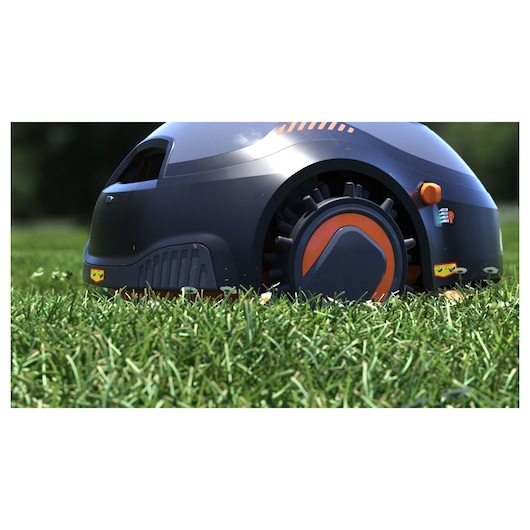 BLACKDECKER BCRMW121 robotic lawn mower side view on grass, dark body with orange accents.