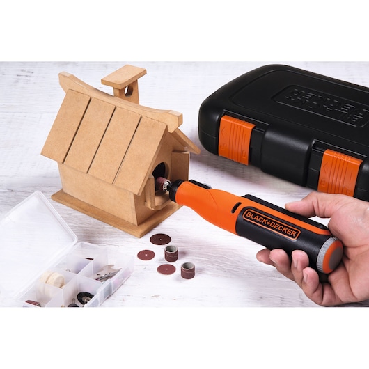BLACK+DECKER BCRT8IK rotary tool used on wooden birdhouse with accessory case and black-orange storage box.