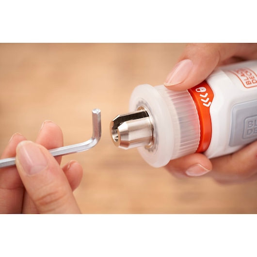 Close-up of a person's hands holding a BLACK+DECKER tool with a metal chuck, using an L-shaped hex key for adjustment or installation.