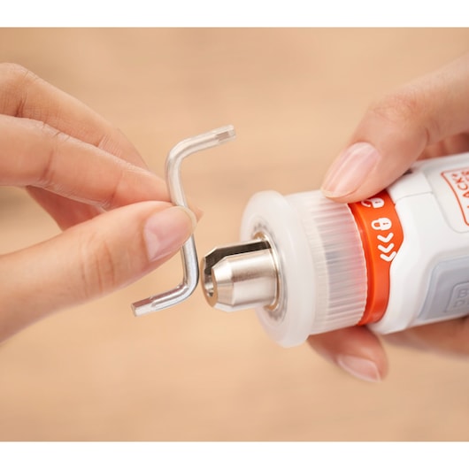 Close-up of hands holding an L-shaped hex key and a BLACK+DECKER rotary tool, showing the insertion or removal of a bit from the tool.