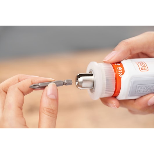 Close-up of hands holding a BLACK+DECKER tool, with one hand inserting a screwdriver bit into the tool's chuck.