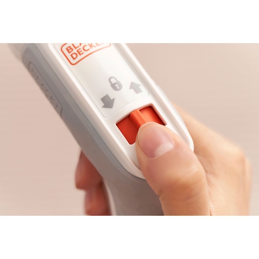 Close-up of a hand pressing an orange switch on a BLACK+DECKER device, with lock and arrow symbols indicating operational instructions.