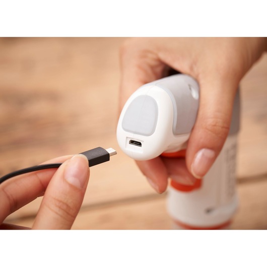 Close-up of a person about to insert a USB charging cable into the port of a handheld device with a white and gray body.