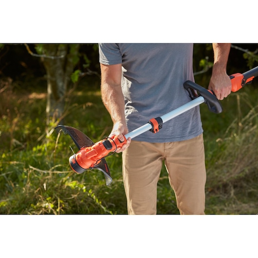 Photo of BLACKDECKER BCSTA536B grass trimmer in use outdoors, orange and black tool with adjustable shaft.